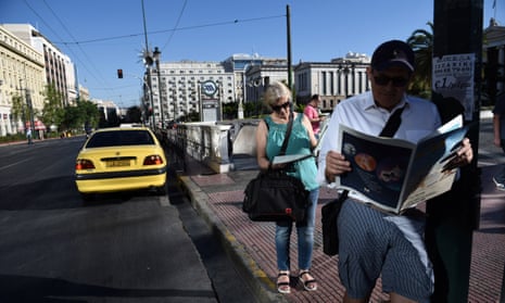 Commuters read newspapers as they wait at a bus stop in Athens this morning.