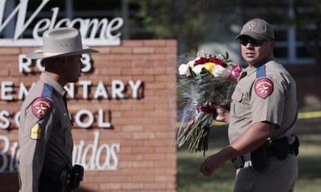 A Texas state trooper carries flowers near the Robb elementary school after a mass shooting at the school that killed 19 children and two adults.