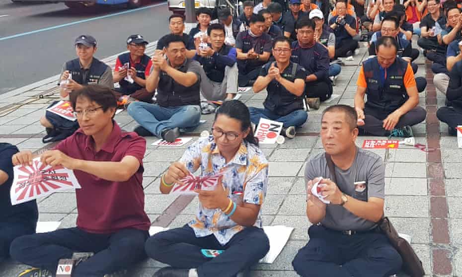 South Korean protesters clap and tear leaflets bearing Japan’s rising sun symbol on hearing that the intelligence sharing pact will end.
