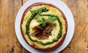 A round terracotta dish of shepherd's pie on a round white plate