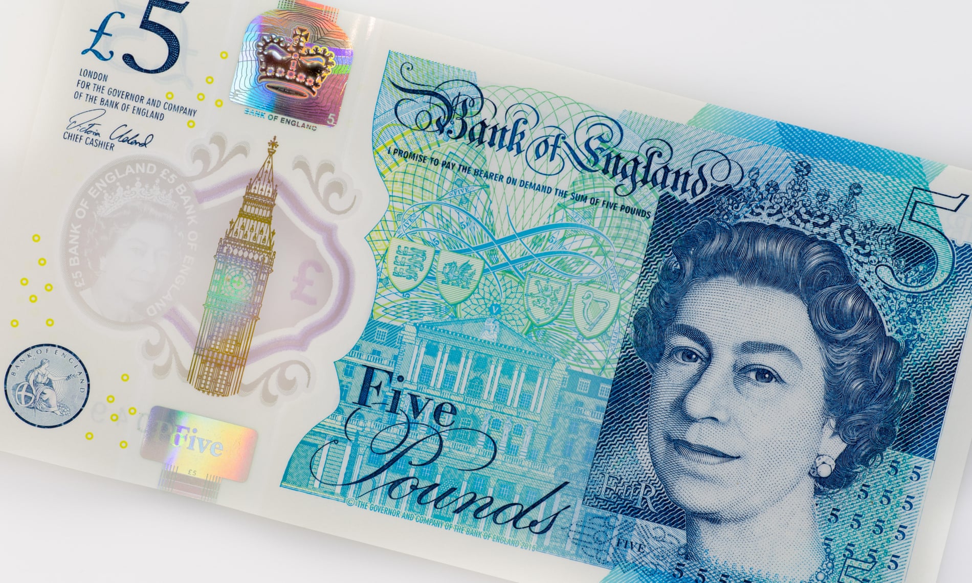 Primer plano de un billete de cinco libras esterlinas del Banco de Inglaterra. En el billete se muestra un retrato de la Reina Isabel II a la derecha, con detalles en tonos azules y verdes. A la izquierda, se ve una ilustración del Big Ben y varios elementos de seguridad, como un holograma y microimpresiones. En la parte superior izquierda se encuentra el símbolo de la libra esterlina (£) y el valor del billete (5). En el centro, el texto "Bank of England" y "Five Pounds".