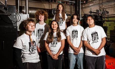 Six middle school-age kids pose in white T-shirts with black Youth vs Apocalypse logos pose before machinery at Melrose Learning academy in Oakland, California.