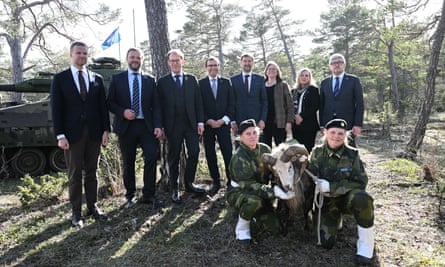 Politicians stand in woodland as a two armed forces personnel hold a regimental goat
