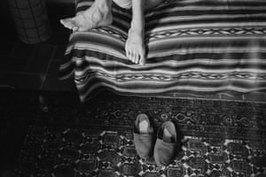 Bare feet seen on a bed from above, and a pair of shoes on the carpet beneath