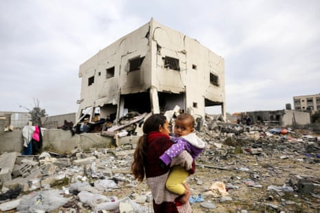 a girl holds a baby amid rubble