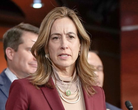a woman speaks at a news conference with people visible behind her