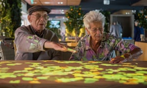 Lights are projected on to a table as two people with dementia use Tovertafel (Magic Table).