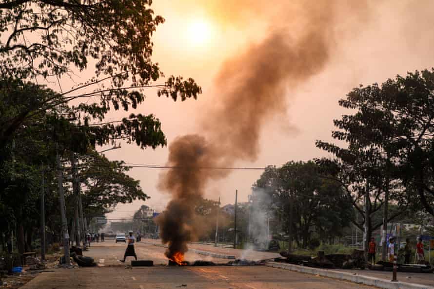 A protester walks past a burning makeshift barricade in Hlaing Tharyar township.