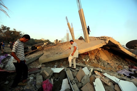 Under a clear blue sky, men walk on the top of the rubble of buildings.