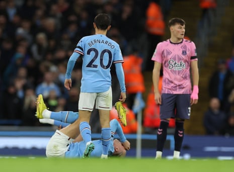 Manchester City's Erling Haaland grimaces in pain as his teammate Bernardo Silva retrieves his boot.
