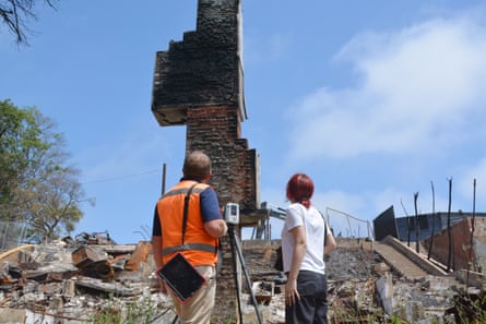 two people stand by chimney standing alone next to piles of debris