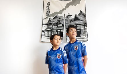 Iena and Yuji Mirto wearing blue Japan shirts and standing in front of a hanging depicting a pagoda