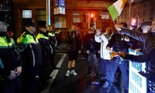 Anti-immigrant protesters wave Irish flags while confronting line of police officers