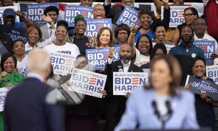 two blurry people in front of crowd holding ‘Biden Harris’ signs