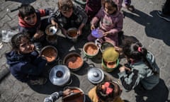 Palestinian children, with filled containers, sit on the ground after waiting in a line for food in Rafah. (Photo by Abed Zagout/Anadolu via Getty Images)