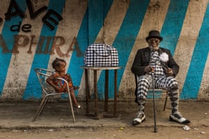 Yamea Bansimba Jean Claude, 58-year-old bricklayer and sapeur for 50 years, in Brazzaville. True sapologie is about more than expensive labels: the art lies in a sapeur’s ability to put together an elegant look that is unique to their personality. Yamea Bansimba Jean Claude wears a jacket by Point De Rue, trousers and shirt by Giorgio Armani, unbranded bow tie and French-style pipe, glasses by Cartier, walking cane by Vermeiren, Italian-style socks and shoes by JM Weston