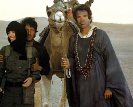 Two men and woman smile with camel outside