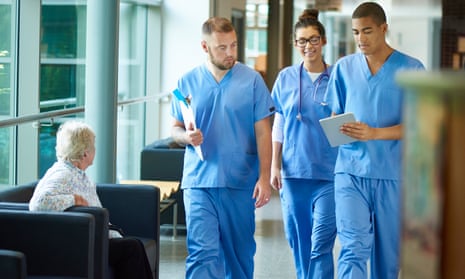 Three junior doctors walking along a hospital corridor discussing case and wearing scrubs.