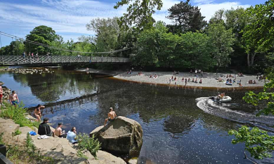 People sunbathing and paddling in the River Wharfe in Ilkley in June