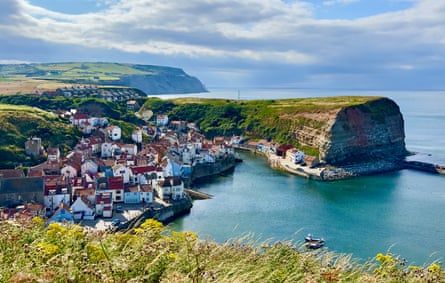 An elevated view of a traditional historic fishing village, with colourful cottages tumbling down the hillside to the sea and harbour.