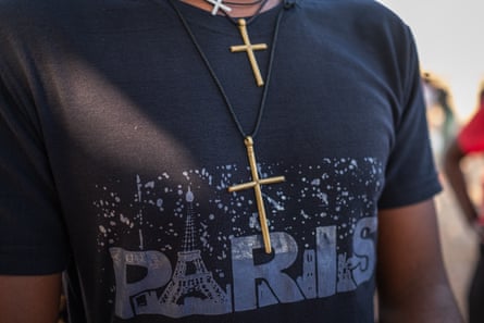 Two gold crosses hang on a man’s chest over a T-shirt that reads ‘Paris’.