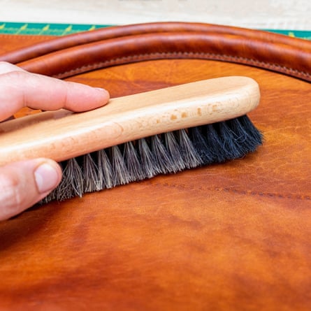 A close up of a hand Polishing handmade leather bag with brush and wax