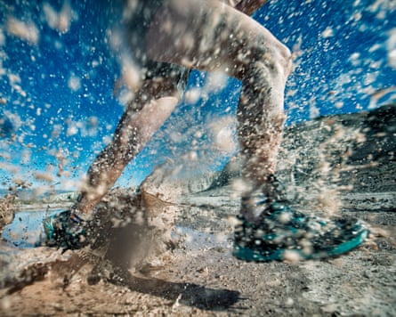 A trail runner runs and splashes through mud and water on a desert trail. There is a lot of mud coming towards the lens.
