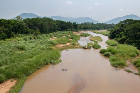 A body of water in a green setting, with trees and hills in the background