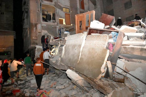 Orang-orang berkumpul di lokasi bangunan yang runtuh di Hama, Suriah.