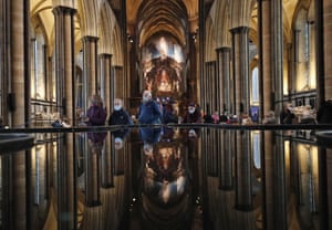 People are reflected in the water of the font inside Salisbury Cathedral as they leave after receiving their Pfizer/BioNTech vaccination.