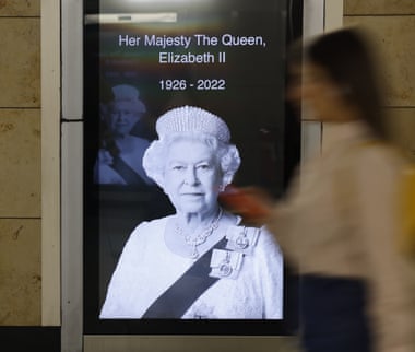 Poster of the Queen in a London underground station with a woman walking past it