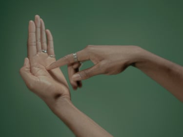 Close-up of two hands touching fingertips, against a soft green background