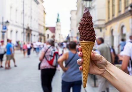 A hand holding a dark chocolate ice-cream on a street.