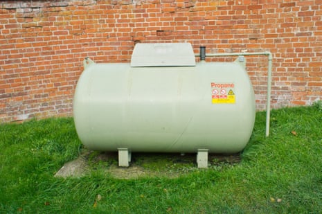 A large propane tank against a red brick wall.