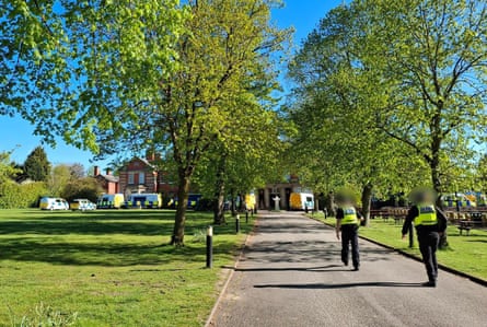 Officers walk along a long tree-lined driveway towards the building