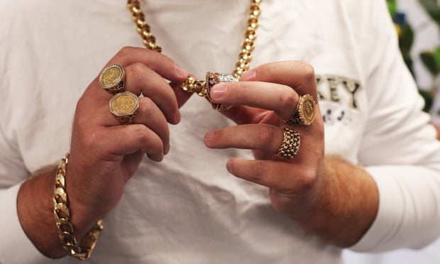 closeup of person showing hands with huge gold rings and big golden chain necklace and bracelet
