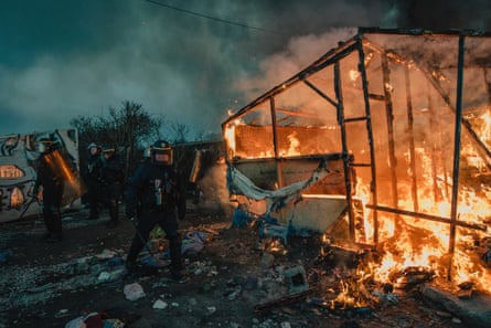 French police try to push refugees away from a fire