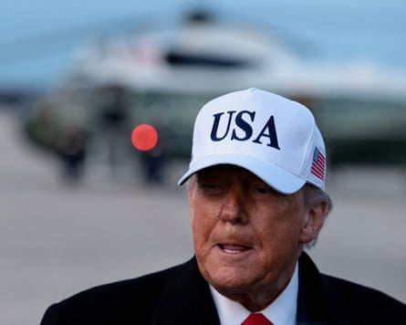 Donald Trump wearing a white baseball cap that says USA on the front and has a US flag on the side