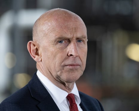 Chancellor John Healey, in a dark suit and red tie, looks seriously at the camera