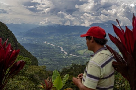 A man in a red cap looks out over a green mountain valley.