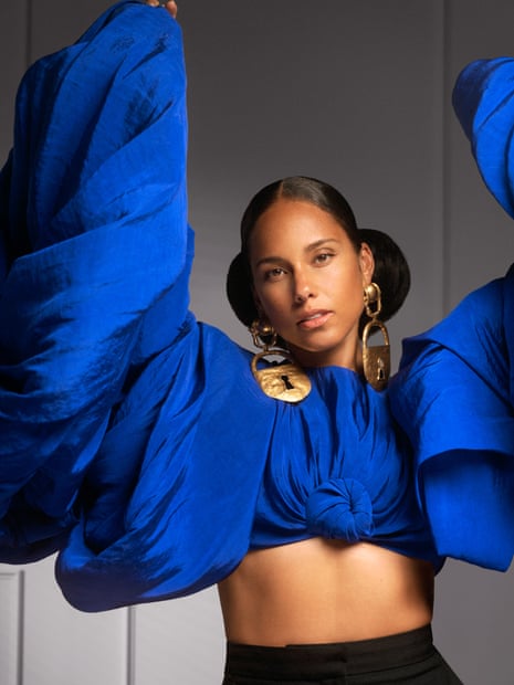 Alicia Keys in a vibrant blue outfit with voluminous sleeves wears large gold padlock earrings