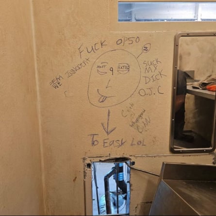 A window-size hole in the wall of a jail cell with profane message taunting authorities