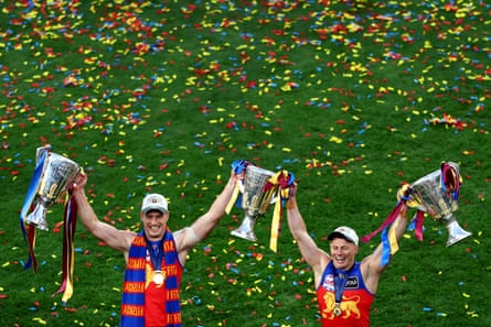 Jarrod Berry and Dayne Zorko hold the 2024, 2025 and 2026 between them with blue, red and yellow confetti covering the MCG grass behind them