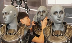 Three bionic humanoid robots. A technician pulls the face covering over one of them