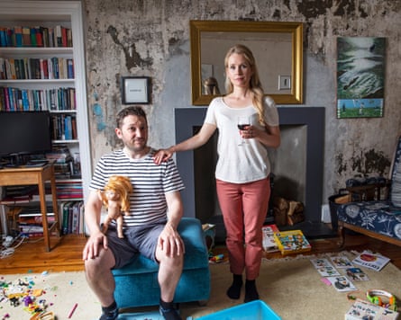 Comedians Jon Richardson and Lucy Beaumont pose with a doll and wine in a worn living room