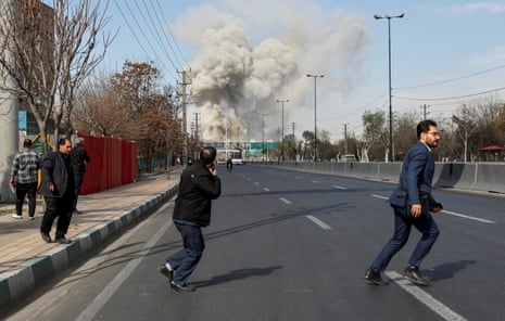 People run for safety after an airstrike in central Tehran, as smoke rises near a major road.