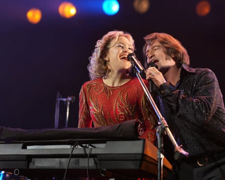 A woman in a red dress and a man in a sparkly blue shirt singing on stage.