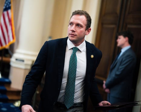 Rep. Max Miller, in a dark suit and green tie, glances upward while walking through a hearing room