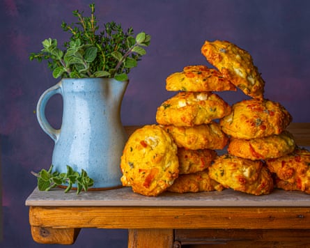 A stack of scones on a wooden table next to a blue jug with mint in it.