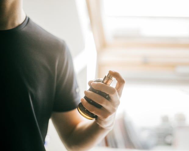 A young man sprays perfume on himself from a glass bottle